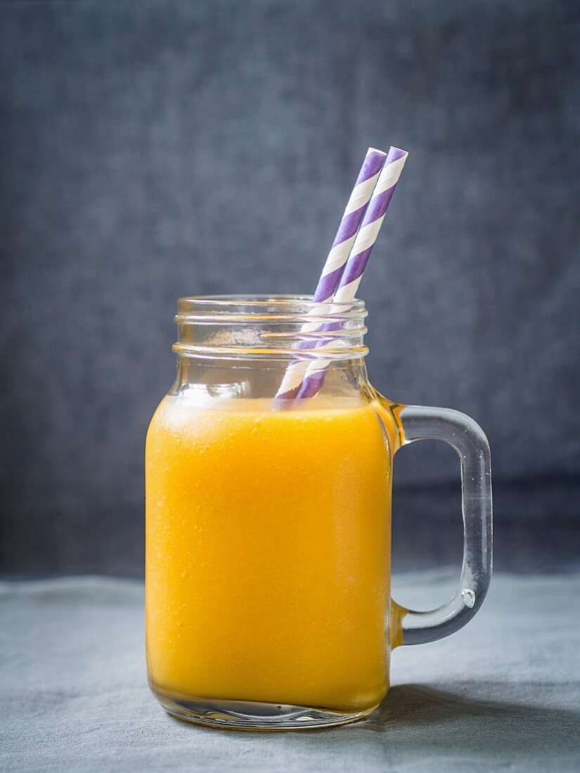 Gelber exotischer Fruchtsmoothie in einem Glas mit Papierstrohhalmen