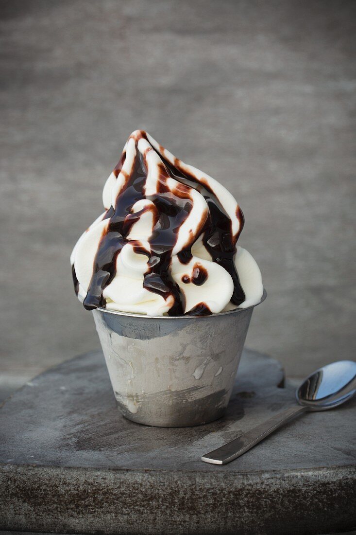 Frozen yoghurt in a metal cup with chocolate sauce