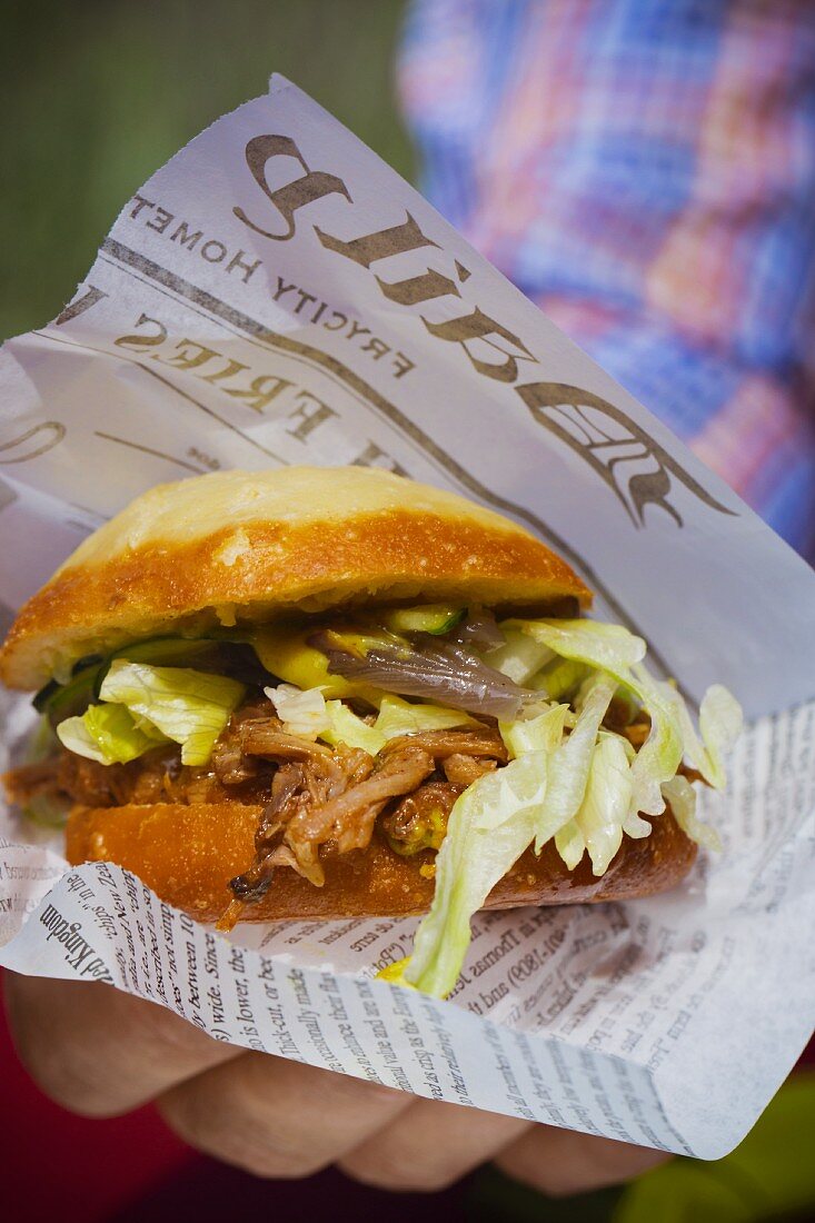 Pulled Pork Burger mit Salat und Schmorzwiebeln in der Hand eines Mannes