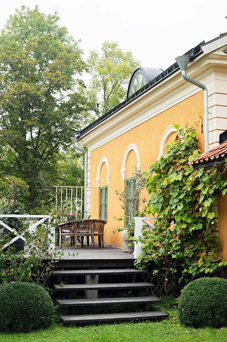 View from garden to steps and terrace outside traditional country house painted yellow with stucco façade elements