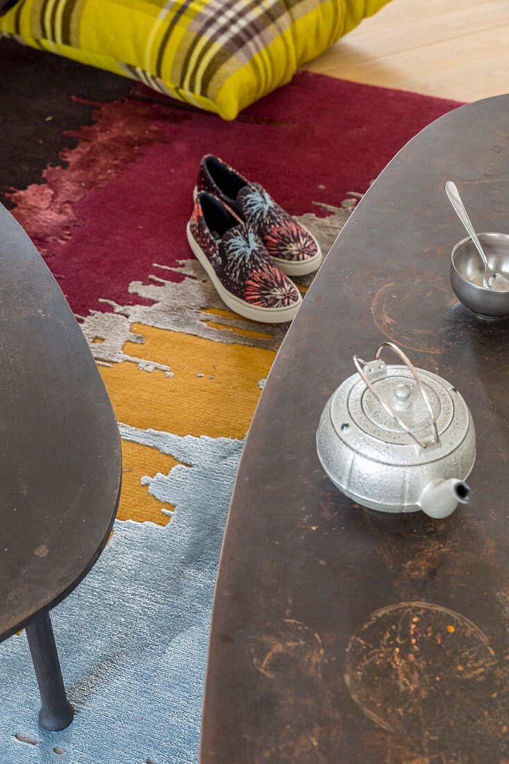 Vintage teapot on coffee table above slip-on sneakers on colourful rug