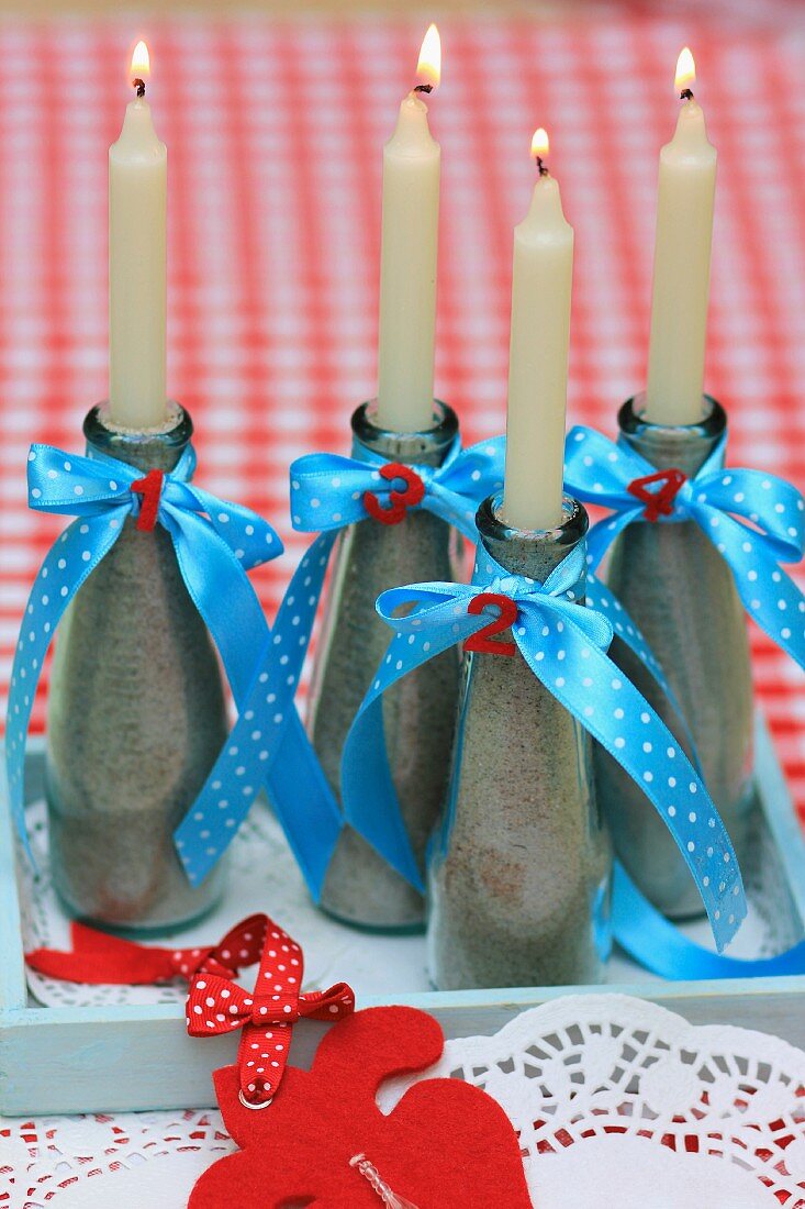 Candle holders made from bottles filled with sand and decorated with ribbons & decorative numbers