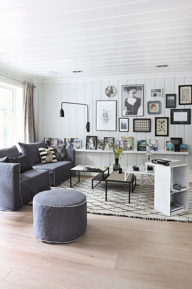 Scandinavian interior with white wood-clad walls, grey armchairs and pouffe next to set of coffee tables