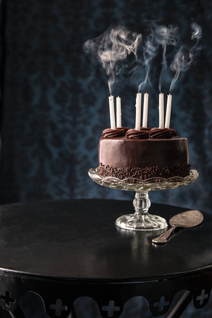 A chocolate cake with blown-out birthday candles on a cake stand