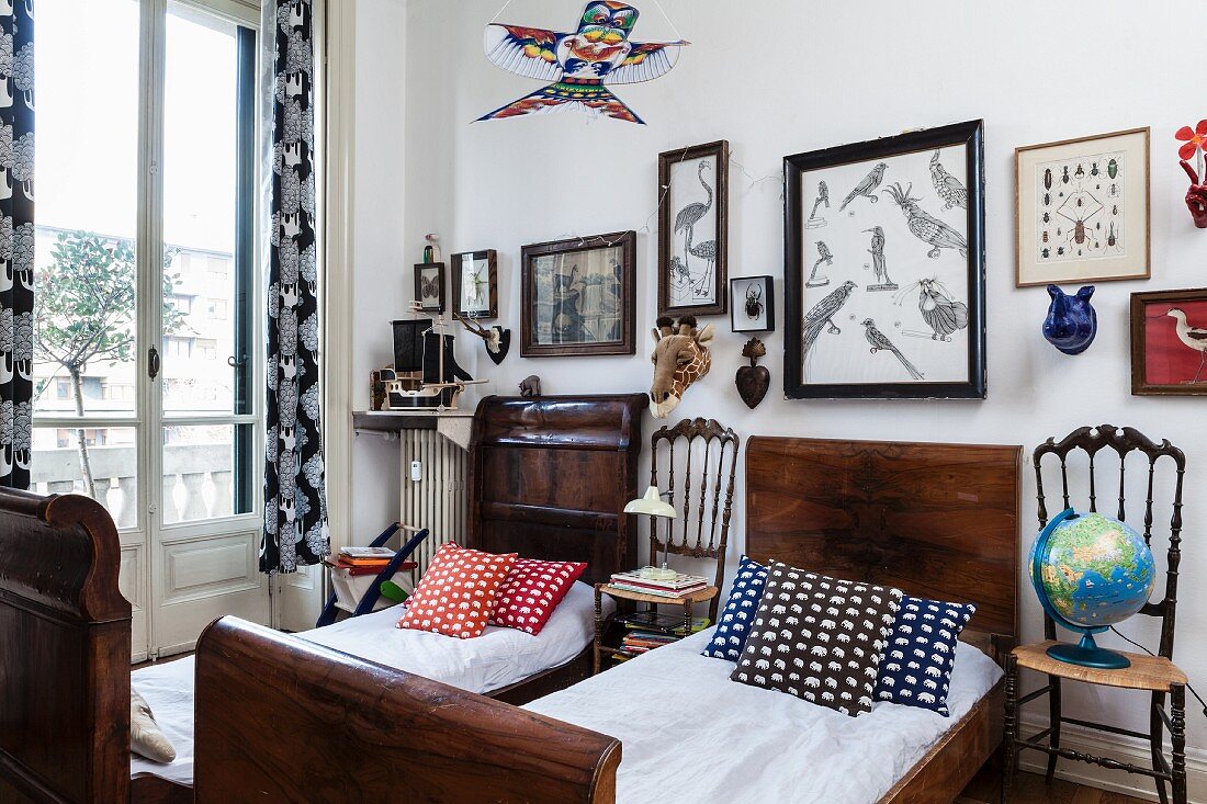Patterned scatter cushions on twin, antique sleigh beds made from dark wood and chairs used as bedside tables below framed pictures of birds on wall