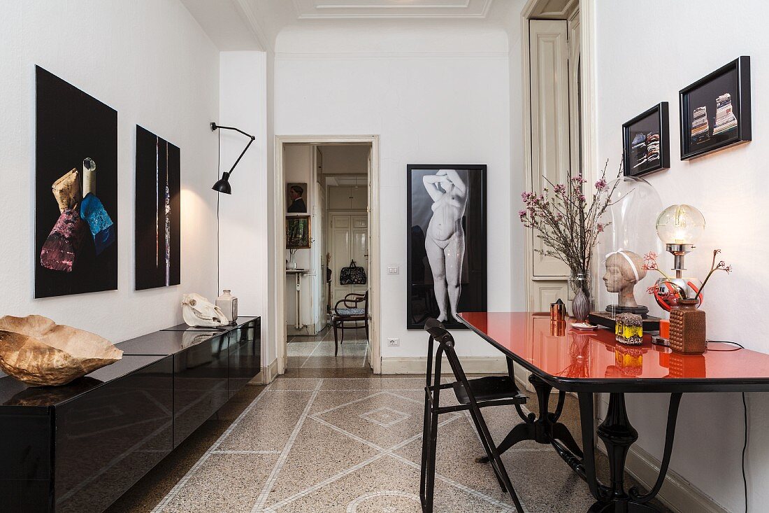 Desk with polished red top and black sideboard in study with terrazzo floor and nude on wall in background