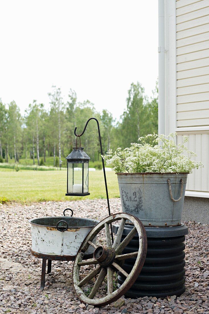 Arrangement of zinc buckets, cartwheel and lantern in garden