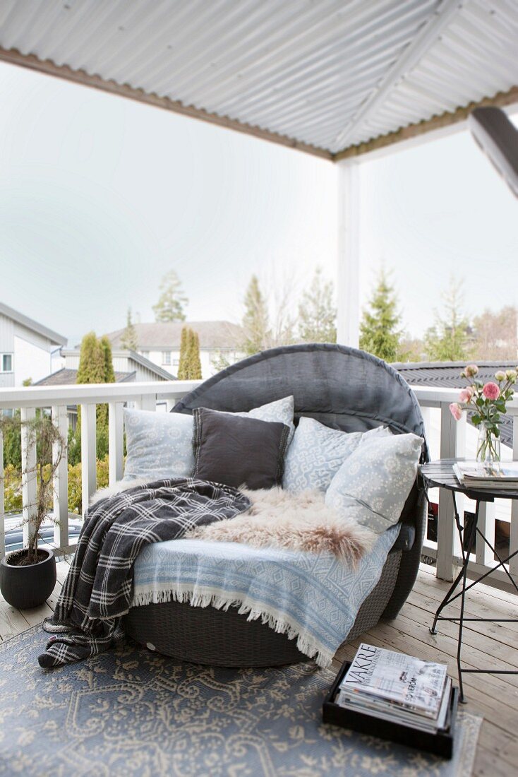 Loungesessel mit Kissen, Fell und Decken auf einer überdachten Terrasse