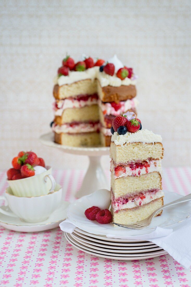 An Eton Mess layer cake with strawberries, raspberries and blueberries, sliced, with a slice on a plate