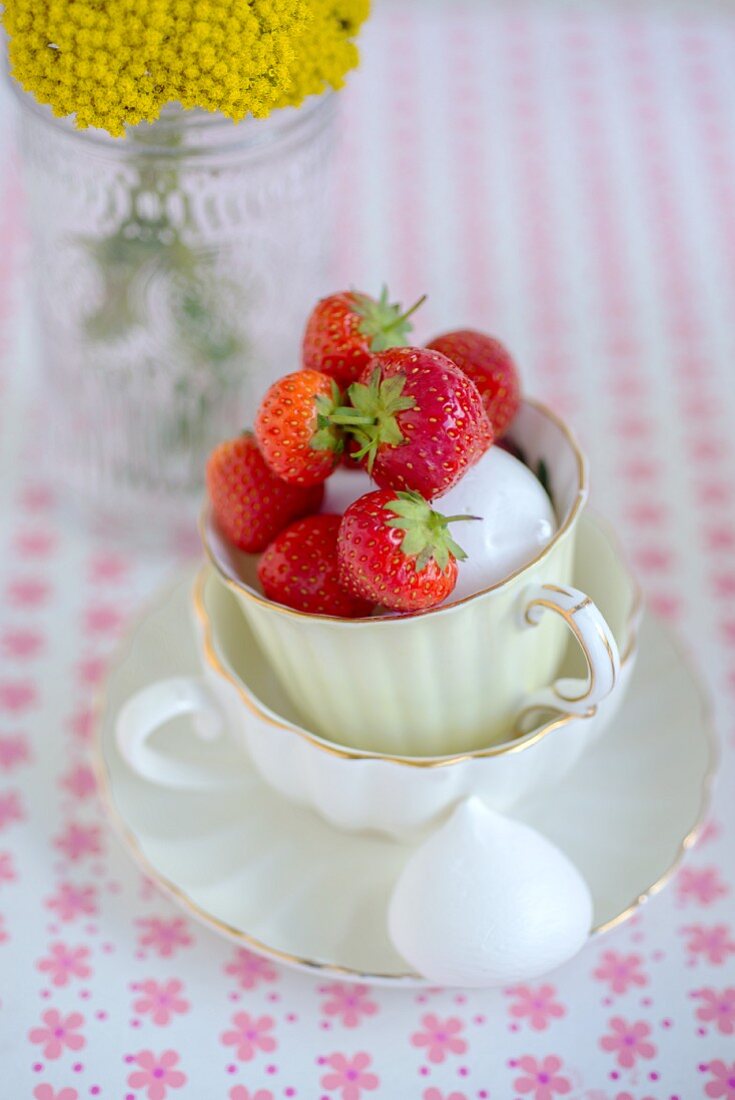 Erdbeeren und Baiserküsse in Teetassen auf geblümtem Untergrund