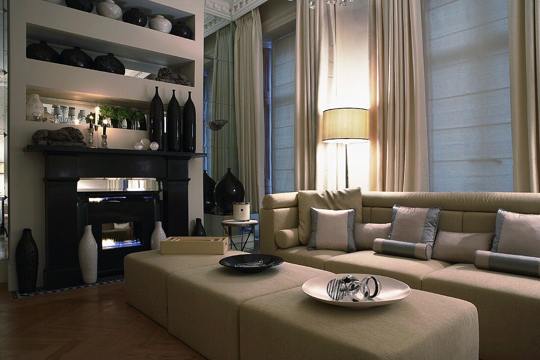 Three ottomans in front of classic sofa and collection of vases on elegant, mirrored shelves above fireplace