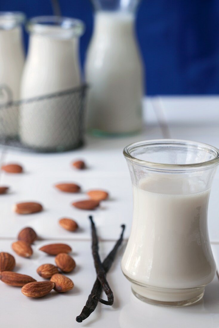 A glass of almond milk with vanilla pods and whole almonds
