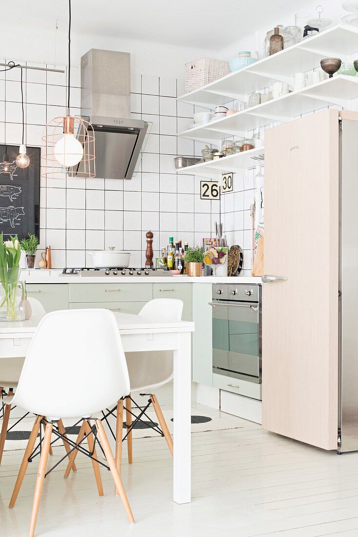 White classic chairs around table and retro fridge in open-plan fitted kitchen with white-tiled walls