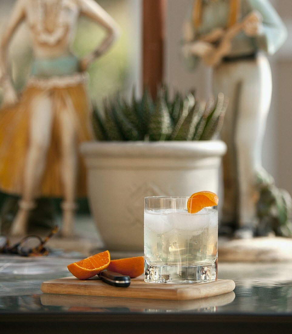 A glass of ginger beer with ice and an orange wedge