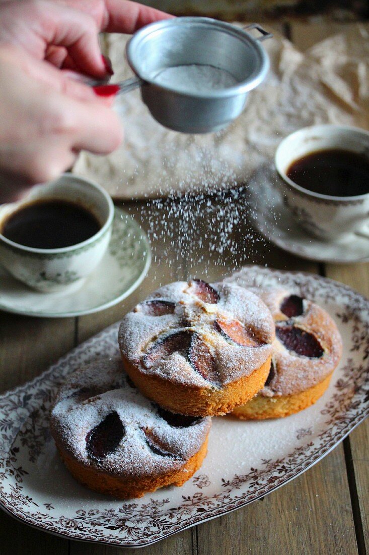 Hands sprinkling a plum and apple cake with icing sugar