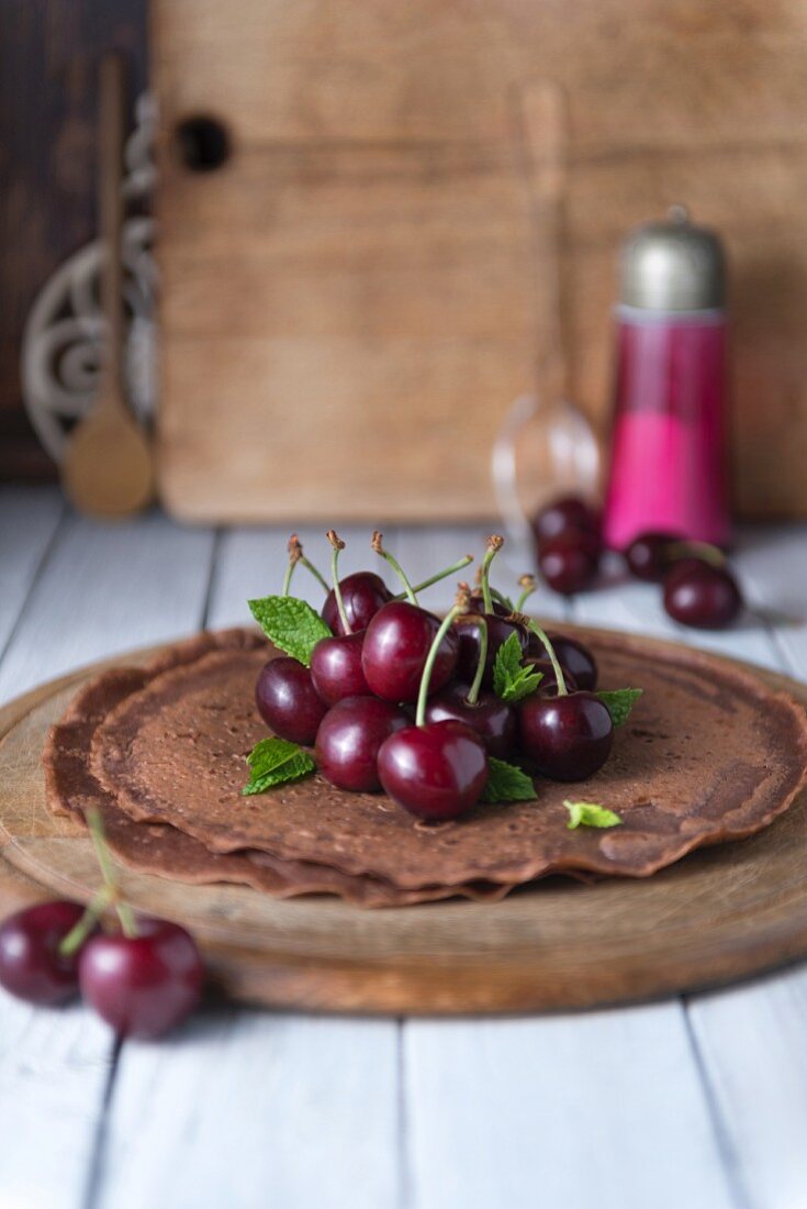 Chocolate crepes with cherries on a wooden plate