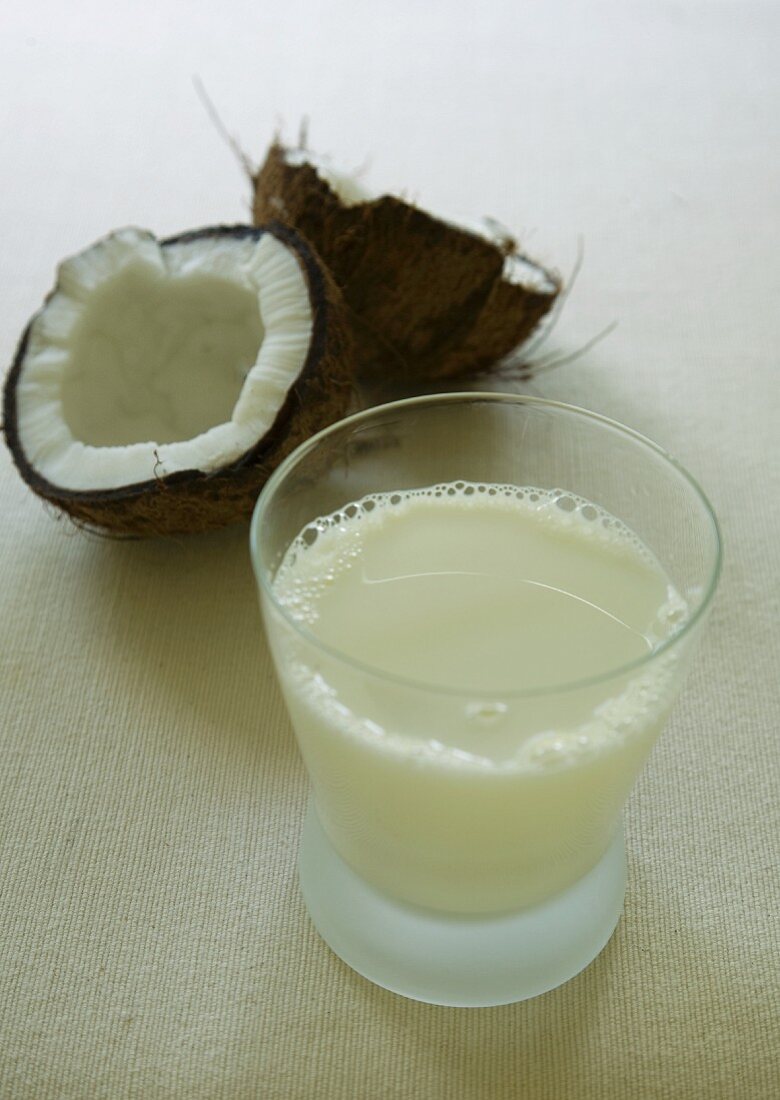 A glass of coconut milk with a coconut in the background