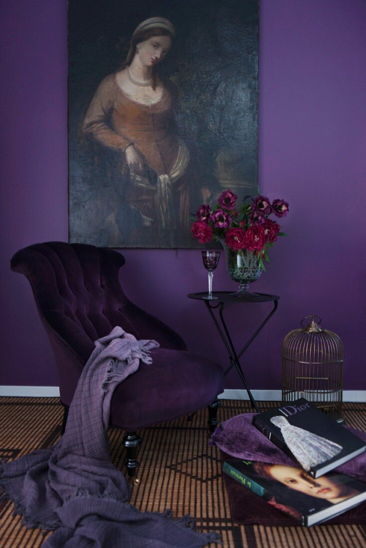 Sessel mit violettem Bezug und Tisch mit rotem Blumenstrauss vor auberginefarbener Wand mit Ölgemälde