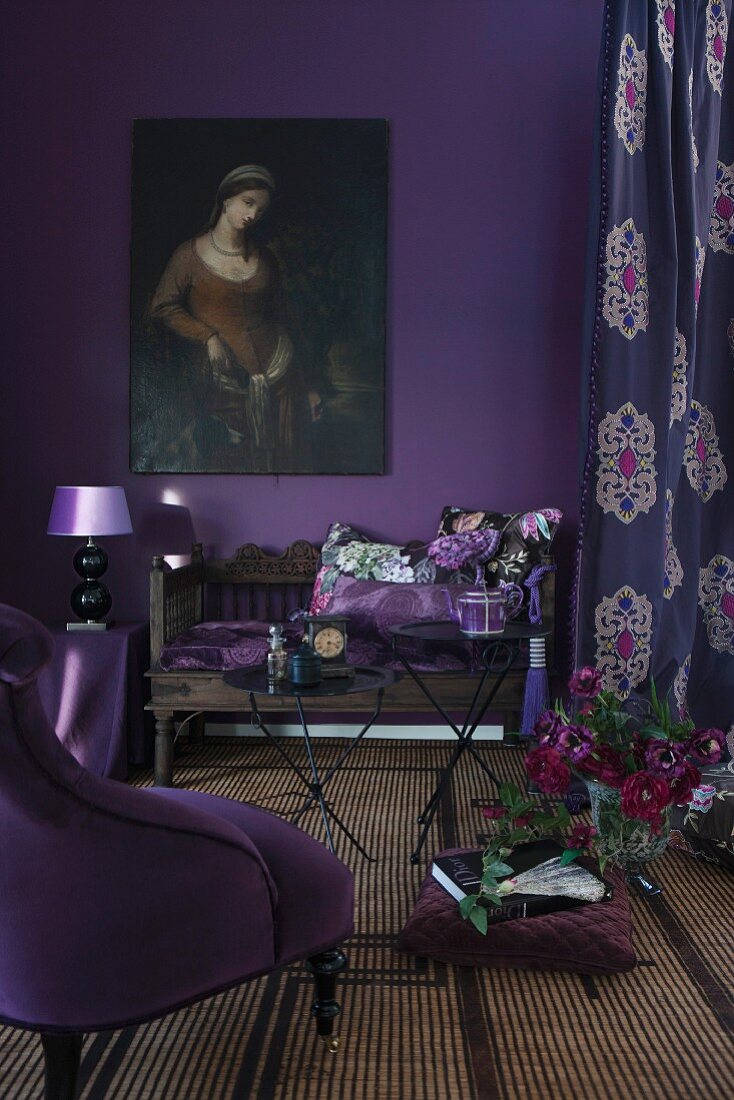 Scatter cushions on antique wooden bench, retro lamp on side table and oil painting of woman on wall painted aubergine