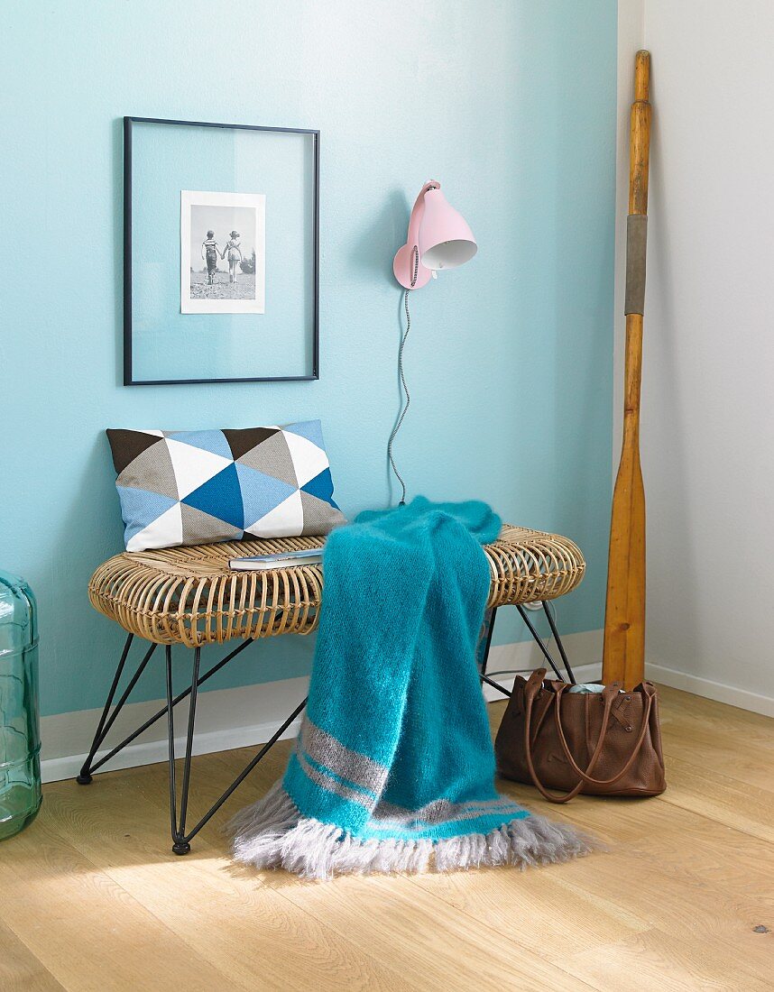 A blue knitted plaid on a 1950s style bench against a pastel-blue wall