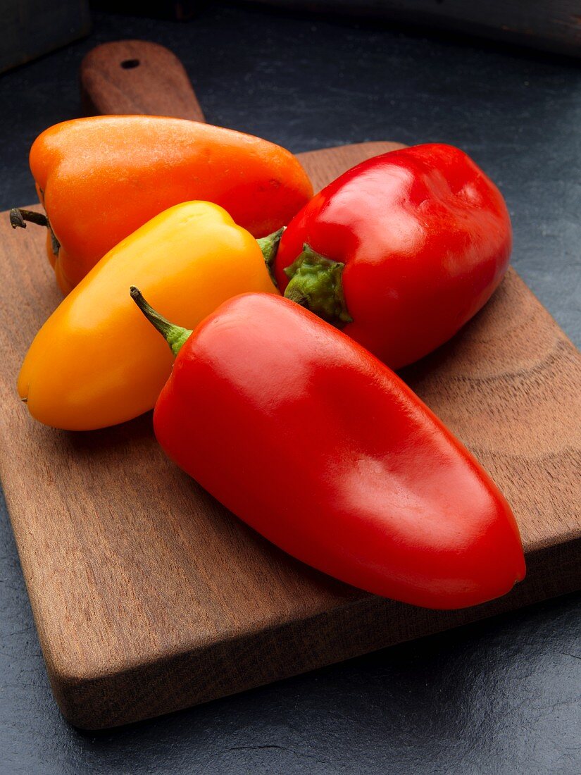 Red, yellow, and orange peppers on a wooden chopping board