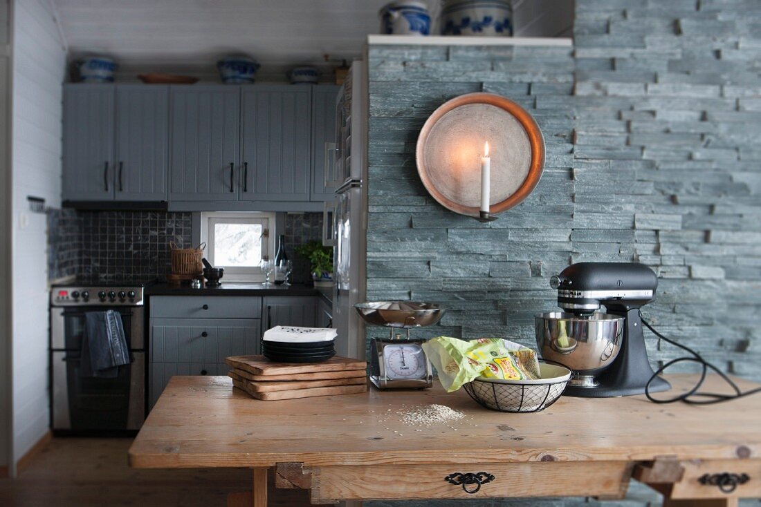 Wooden dining table, candle sconce on stone wall and kitchen integrated into niche