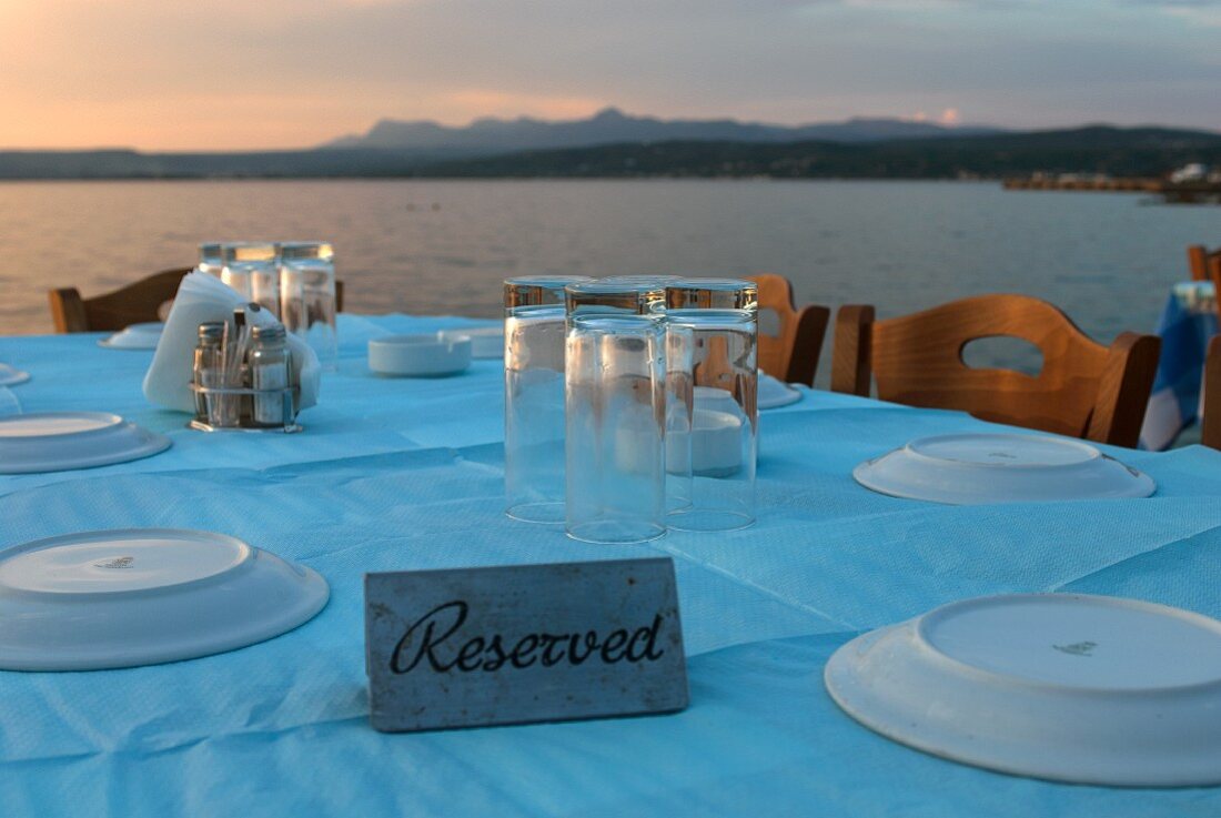 A table laid with a pastel-blue tablecloth with the Greek coast in the background