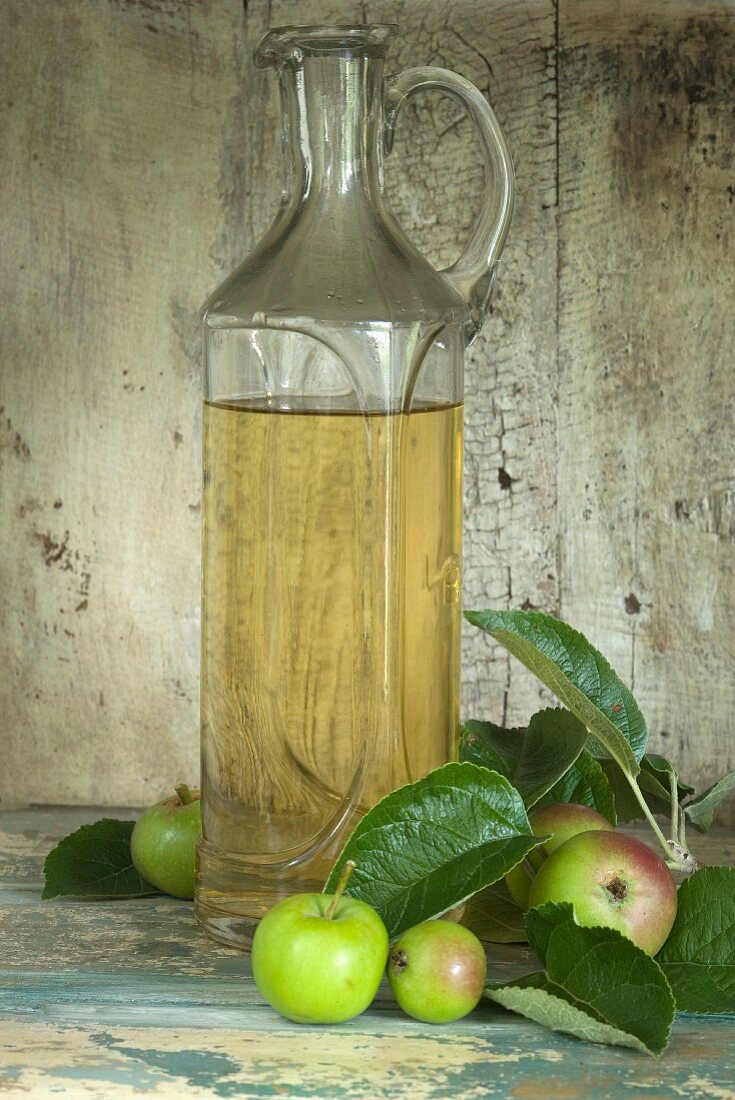 Eine Flasche Apfelessig und mehrere Äpfel in einem rustikalen Schrankfach