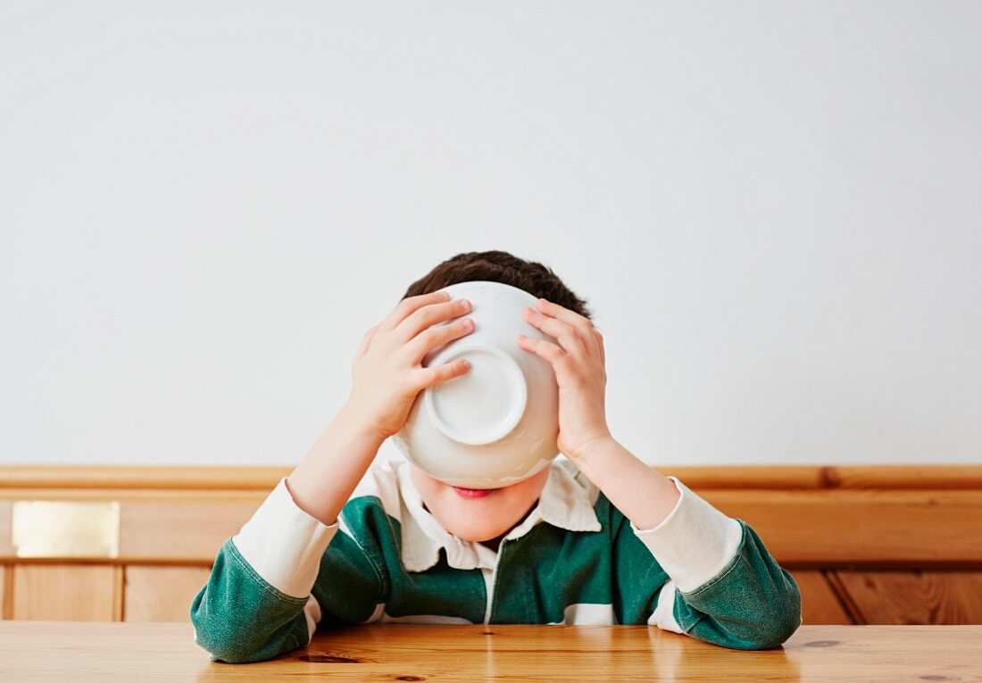 A boy sitting at a table drinking milk from a muesli bowl