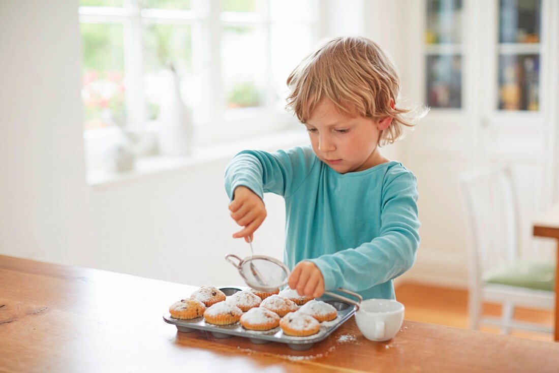 A young boy dusting muffins with icing sugar