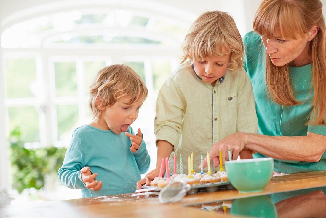 Mutter mit Söhnen beim Verzieren von Geburtstagsmuffins am Küchentisch