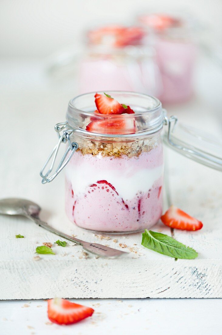Erdbeerjoghurt mit Honig und Minze im Glas auf weißem Schneidebrett