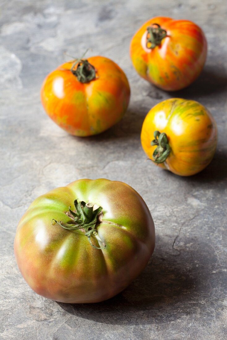 Four organic tomatoes on a stone surface