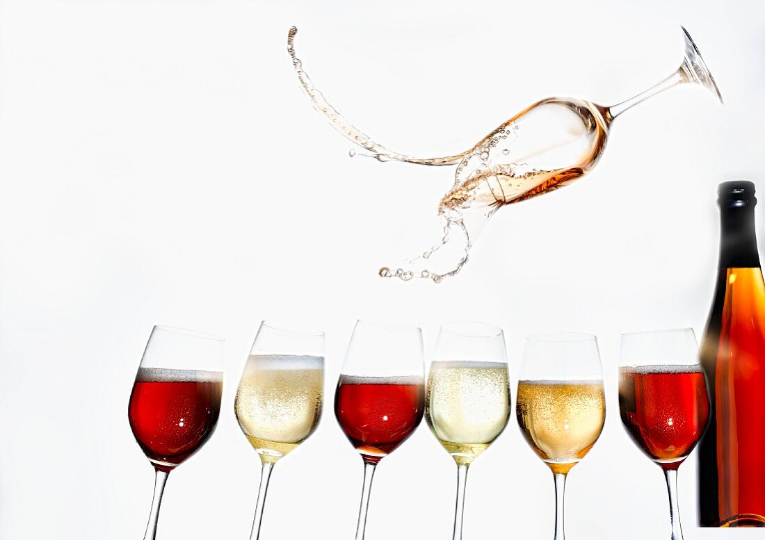 Weingläser mit verschiedenen Fruchtseccos und Flasche, ein Glas darüber schwebend