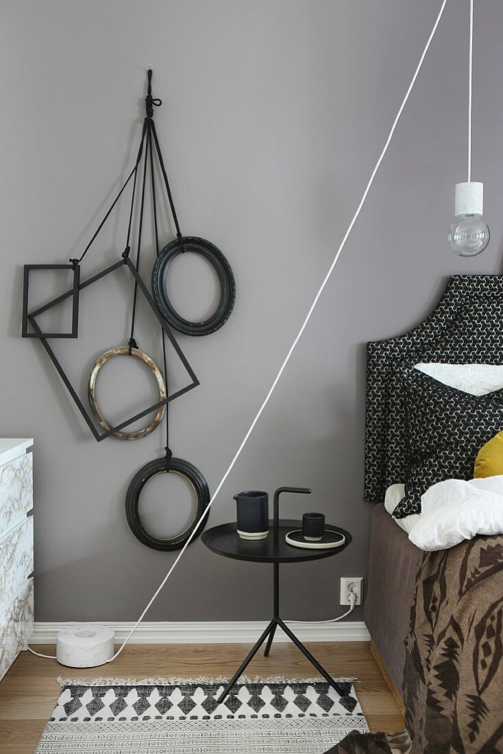Various frames hanging from cords on wall next to bed