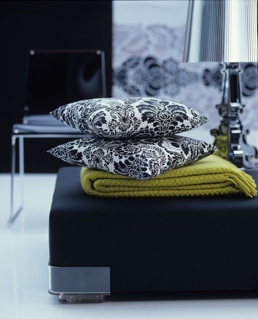 Blanket and black and white, floral scatter cushions on black pouffe in living room