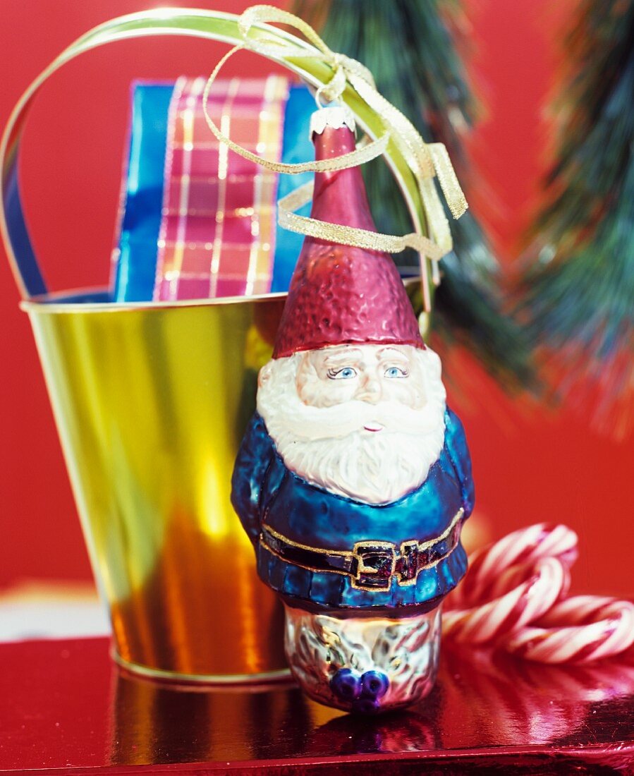 Weihnachtliche Dekoration mit Weihnachtsmann & Geschenk in goldenem Eimer