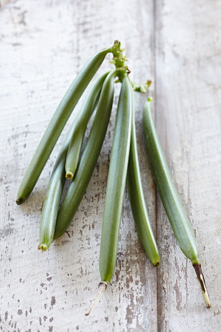 Green vanilla pods on a wooden surface