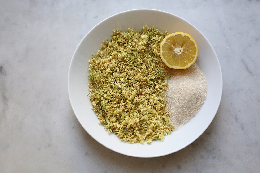 Wilted elderberry flowers with sugar and half a lemon on a plate (seen from above)