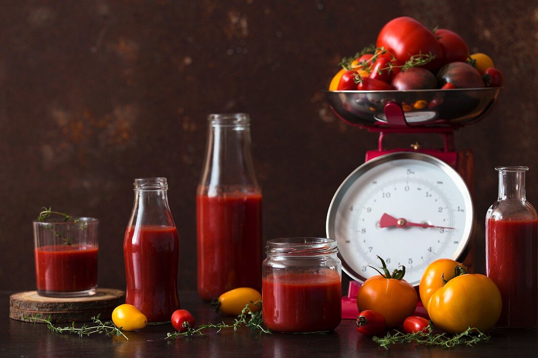 Passierte Tomaten in Gläsern und Flaschen neben frischen Tomaten auf Küchenwaage