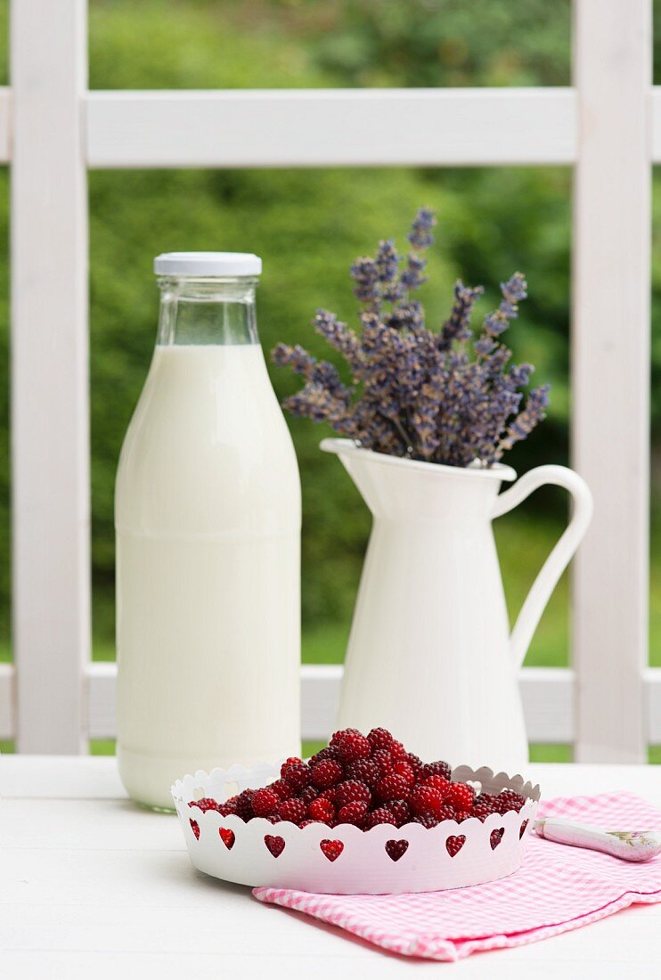 Milchflasche, Lavendel im Krug und frische Beeren auf Gartentisch