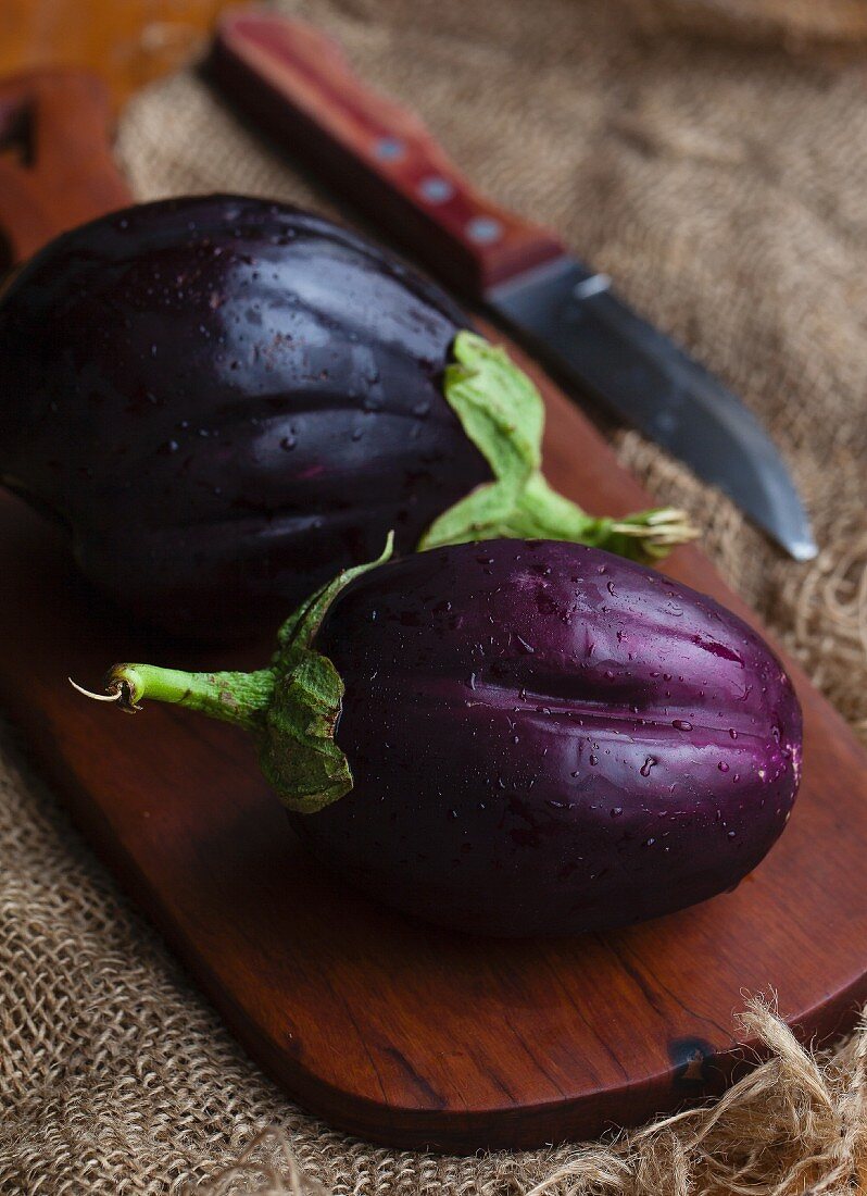 Two fresh aubergines on a wooden board