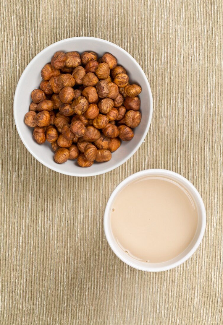 A cup of hazelnut milk and a bowl of hazelnuts