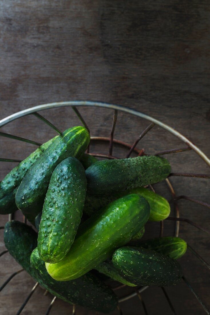 Gherkins in a wire basket on a wooden table top