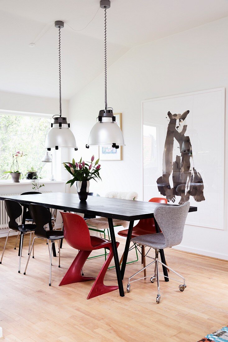 Black retro dining table, two red chairs and industrial pendant lamps in Scandinavian dining room