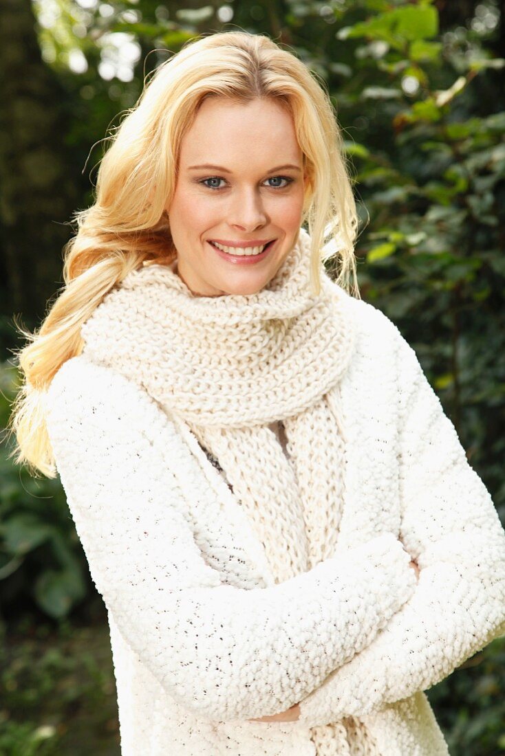 A young woman wearing a white, coarse-knit cardigan and scarf