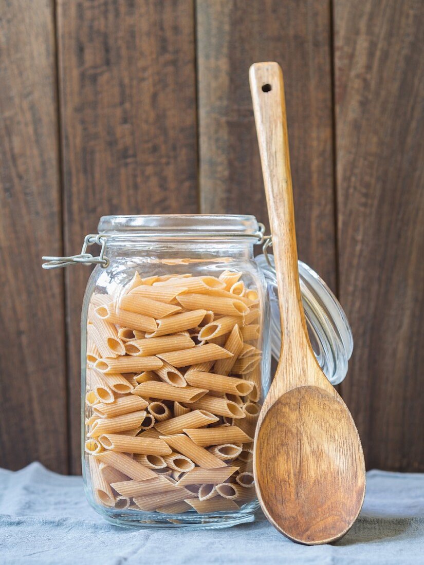 A jar of wholemeal penne with a wooden spoon