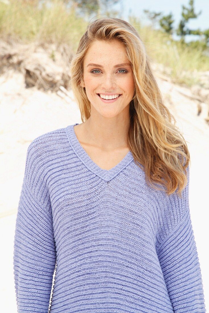 A young woman on a beach wearing a purple jumper