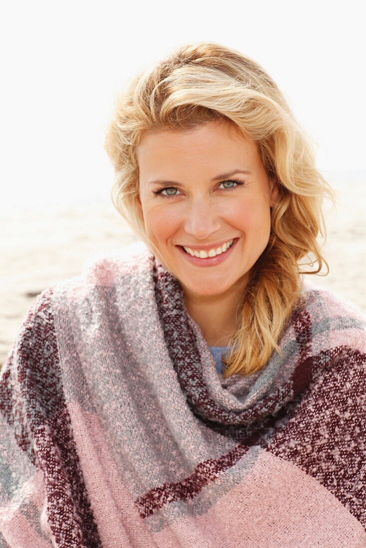 A blonde woman wearing a woollen shawl on a beach