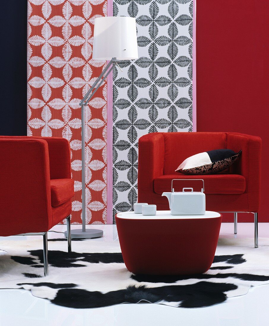 Elegante rote Designersessel mit passendem Couchtisch und weißem Teegeschirr auf schwarzweißem Tierfellteppich, dekorative Wandgestaltung